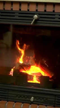 Vertical video: warm cozy fireplace with wood during a cold day at home. Winter and homey concept, static background of a fireplace in vertical format