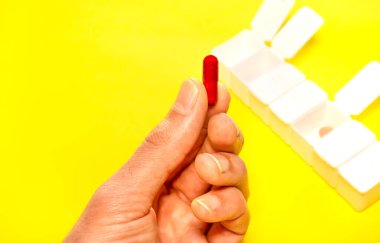 El, sarı arka planda beyaz hap kutusu ve fotokopi alanı olan renkli kırmızı bir hap göster. İlaç, tablet, kapsül kavramı...