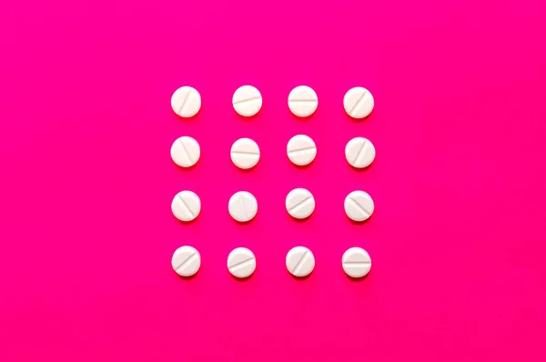 핑크 배경에 한 줄로 놓인 밝은 흰색 알약이나 알약. — 스톡 사진
