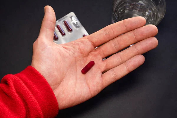 Person taking medication with black background with blister and water. — Stock Photo, Image