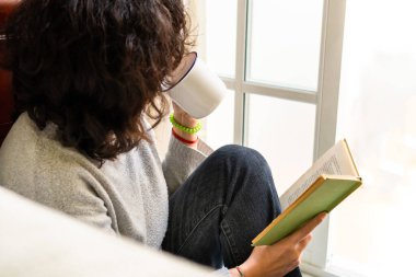 Siyah saçlı, sıradan bir kazak giyen, kahve içen ve evinin penceresinin yanında ilginç bir roman okurken yüzünü çeviren...