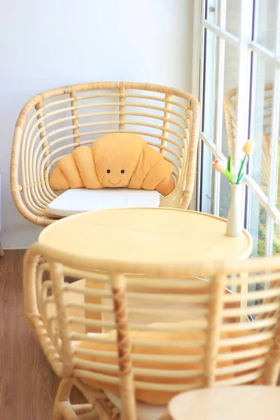 A set of rattan rattan tables and chairs set up in a coffee shop to accommodate customers. There is a doll in the back