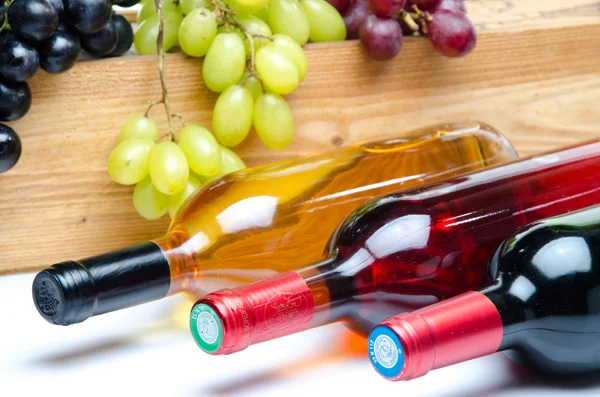 Bottles of wine in front of a wooden box with grapes — Stock Photo, Image