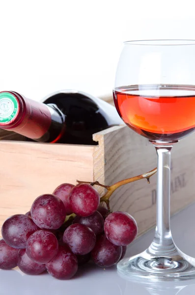 Bottles of wine in a wooden box with a glass of wine and red gra — Stock Photo, Image