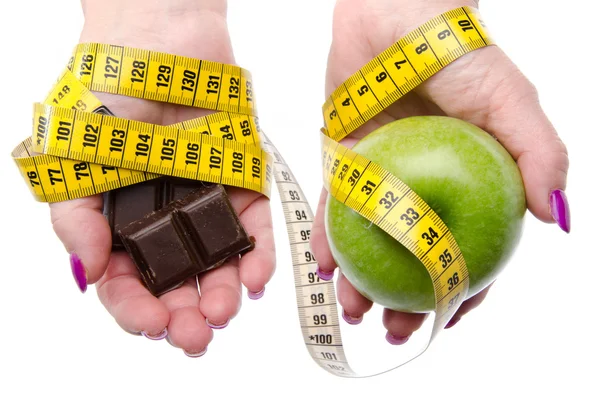 Измерение ленты вокруг женских рук, держащих яблоко и шоколад — стоковое фото