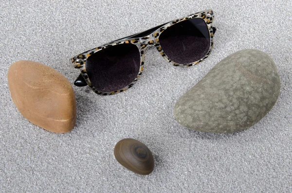 Sunglasses and pebbles on the sand — Stock Photo, Image