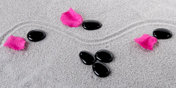Composition of black pebbles with flower petals on the sand — Stock Photo, Image