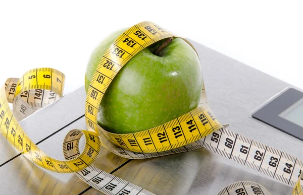 Fita métrica em volta de uma maçã verde em uma balança de banheiro — Fotografia de Stock