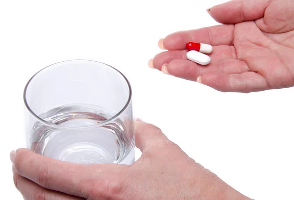 Mãos segurando pílulas e um copo de água — Fotografia de Stock