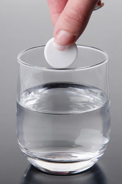 Hand holding a tablet over a glass — Stock Photo, Image