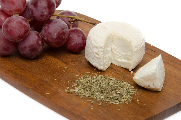 Goat cheese, grapes and provencal herbs on a wooden cutting boar — Stock Photo, Image