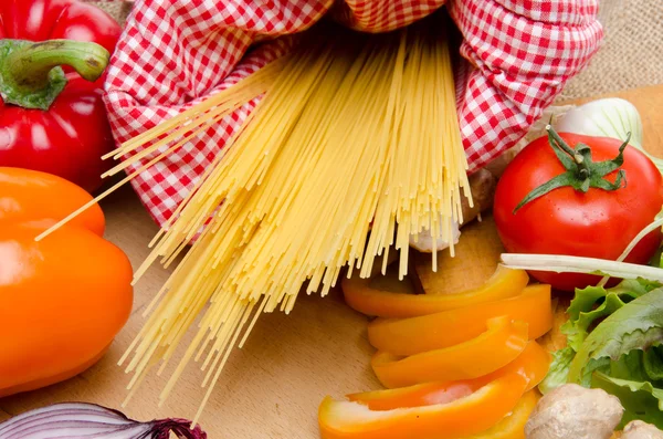 Skład spaghetti niegotowane otoczony warzyw — Zdjęcie stockowe