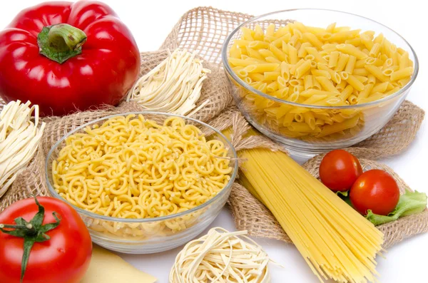 Different types of uncooked pasta and vegetables on a burlap — Stock Photo, Image