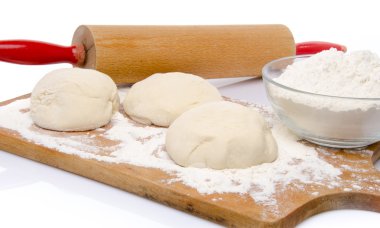 Three balls of pizza dough with a cup of flour and a rolling pin clipart