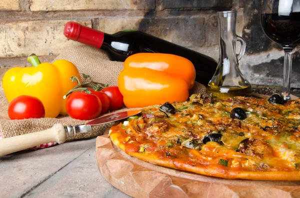 Pizza com vinho e alguns ingredientes em um fundo de tijolos — Fotografia de Stock