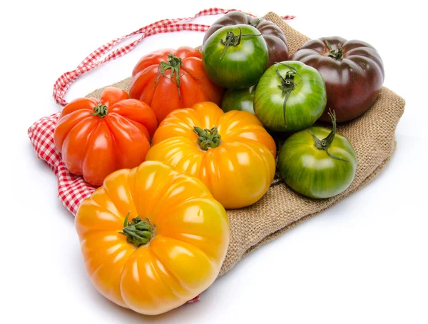 Green, yellow, orange and purple tomatoes on a burlap — Stock Photo, Image