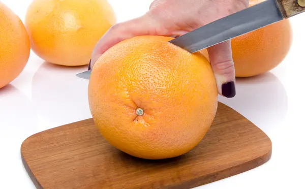 Frauenhand schneidet eine Grapefruit auf einem Holzbrett — Stockfoto