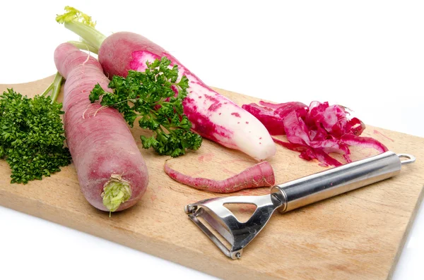 Red radish, parsley and a peeler on a wooden cutting board — Stock Photo, Image