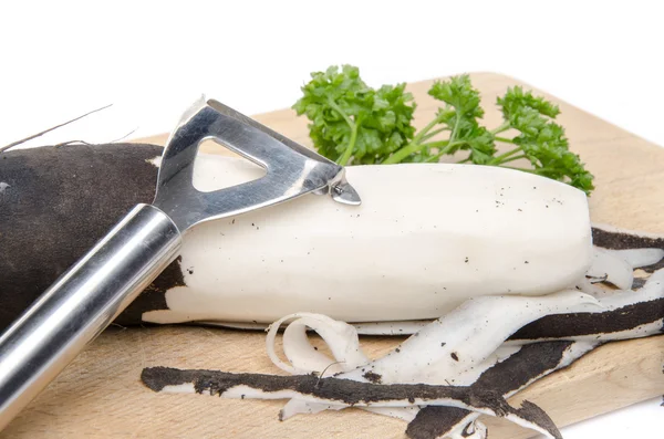 Black radish, parsley and a peeler on a wooden cutting board — Stock Photo, Image