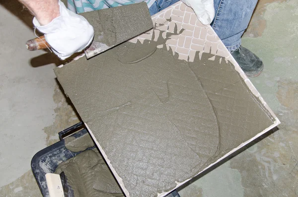 Tiler spreading tile adhesive on the back of a tile — Stock Photo, Image