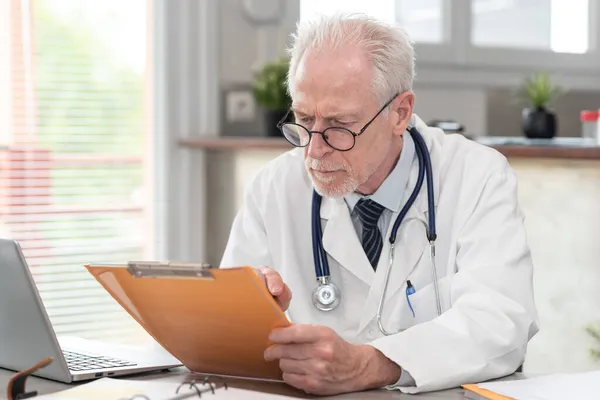 Starší Lékař Čte Klinický Záznam Lékařské Ordinaci — Stock fotografie