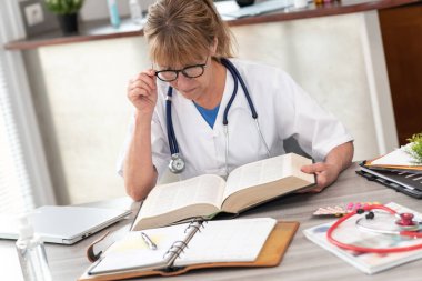 Tıp bürosunda ders kitabı okuyan kadın doktor.
