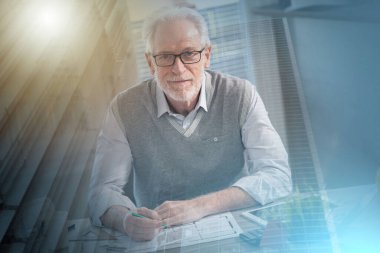 Ofiste oturan ve kameraya bakan kıdemli mimarın portresi.