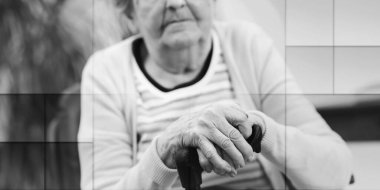 Yaşlı kadın elleri değnekte oturuyor, geometrik desenli.