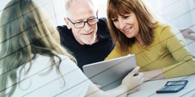 Emlakçı yaşlı çifte tablet üzerinde açıklama yapıyor, geometrik desenli.