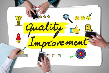 Quality improvement concept placed on a desk with hands using smartphones