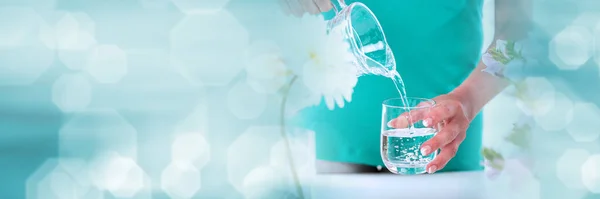 Woman pouring water from a pitcher into a glass; panoramic banner