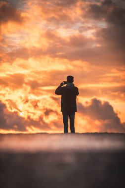 man against the background of an orange sky stands with his back and takes pictures