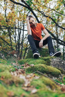 Bir çocuk yeşil bir sonbahar ormanında bir taşın üzerinde oturuyor.