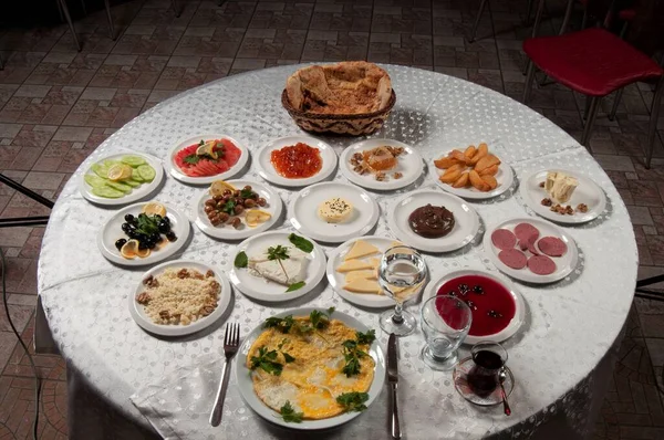 A breakfast table with a variety of foods. There are foods such as eggs, butter, honey, jam, tea, bread, cheese, tomatoes, omelettes on the table.