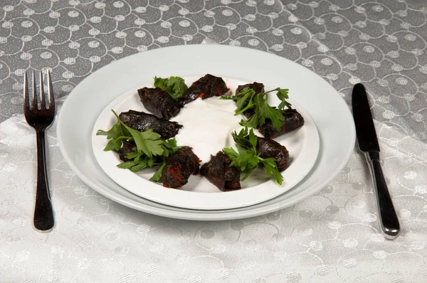 Leaf wrap and yoghurt are on a porcelain plate. Wrapping is made with grape leaves and meat.