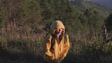Sonbaharda tropikal bir ormanda yürüyüş yapan sarı ceketli genç bir kadın. Sağlıklı ve aktif bir Asyalı kadın gezgin ormanda bir sırt çantasıyla yürüyor..