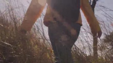 Sırt çantalı mutlu hippi kadın sonbaharda ormanda yürüyüşe çıkıyor. Turist kadın dağ macerasında çayırda yavaşça yabani çimlere dokunuyor..