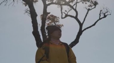 Sarı ceketli bir kadının portresi güneşin doğuşunda dağın tepesinde duruyor ve temiz havayı soluyarak sakin bir günün tadını çıkarıyor..