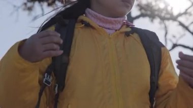 Sarı ceketli, sırt çantalı bir turist ellerini bir dağın tepesinde ısıtıyor. Üşüyorum. Elleri ceketinin cebinde olan bir kadının yakın çekimi.