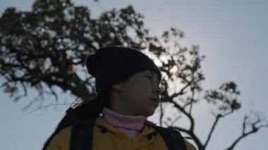 Sarı ceketli bir kadının portresi güneşin doğuşunda dağın tepesinde duruyor ve temiz havayı soluyarak sakin bir günün tadını çıkarıyor..