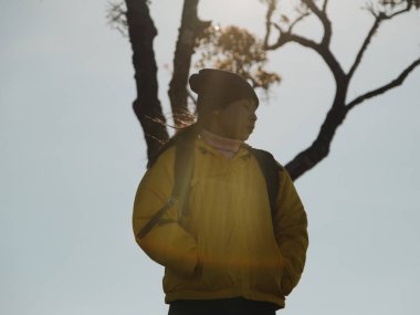 Sarı ceketli bir kadının portresi güneşin doğuşunda dağın tepesinde duruyor ve temiz havayı soluyarak sakin bir günün tadını çıkarıyor..