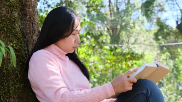 アジアの女子大生は 大学公園の大きな木の下で草の上に座って本を読んでいます 幸せな大人アジアの学生は屋外で勉強 — ストック動画