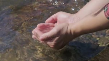 Bir orman nehrinde taze dereleri kepçeleyen ellerin yakın çekimi. Yavaş çekim.