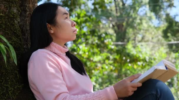 Ázsiai Női Főiskolai Hallgató Gondolkodik Nézi Fát Miközben Olvasás Alatt — Stock videók