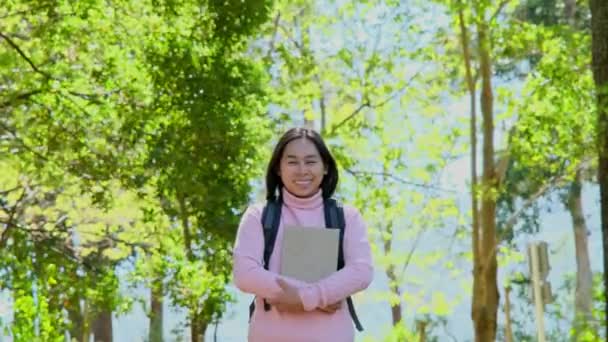 Азійка Студентка Носить Рюкзак Обіймає Книжку Посміхається Камеру Посеред Природи — стокове відео