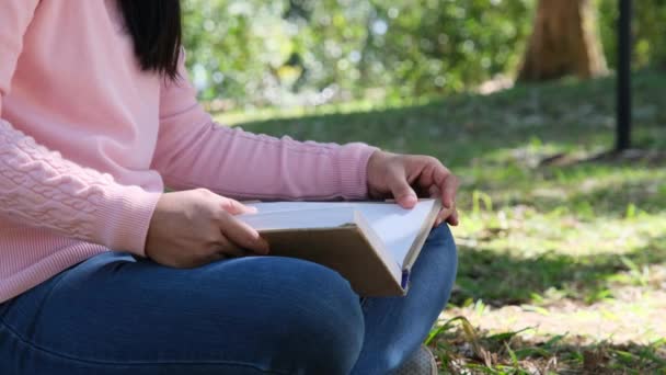 亚洲女大学生正坐在一座大学公园的一棵大树下的草地上看书 快乐的亚洲成人学生在户外学习 — 图库视频影像