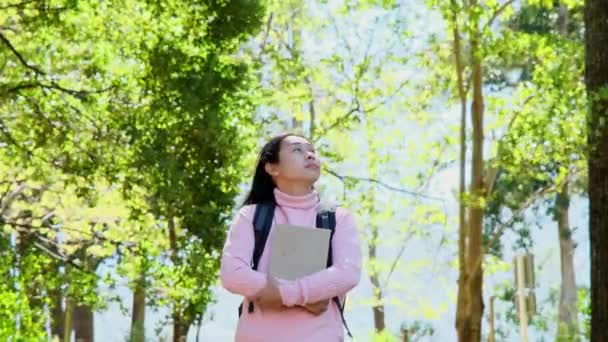 Азійка Студентка Носить Рюкзак Обіймає Книжку Посміхається Камеру Посеред Природи — стокове відео