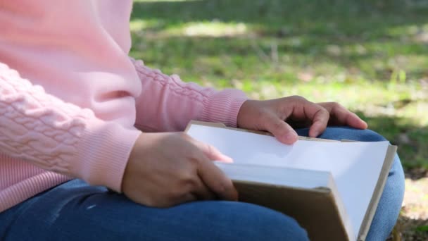 亚洲女大学生正坐在一座大学公园的一棵大树下的草地上看书 快乐的亚洲成人学生在户外学习 — 图库视频影像