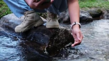 Kadın eli nehirde soğuk suya dokunuyor. Seyahat eden kadın bir kayanın üzerinde duruyor ve elleriyle bir dereye dokunuyor. Elin yakın çekimi.