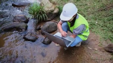 Çevre mühendisleri su kalitesini doğal su kaynaklarında inceler ve verileri dizüstü bilgisayarlara kaydederler. Kadın bilim adamı ve çevre sorunları. Dünya çevre günü kavramı.